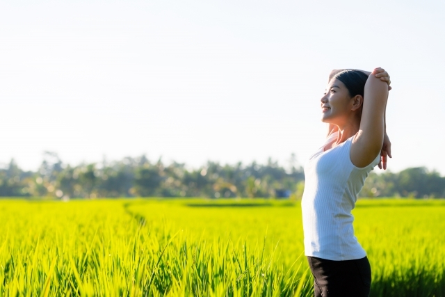 田んぼの前で伸びをする女性